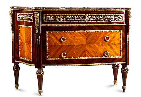 A Louis XVI style gilt-ormolu mounted quarter veneered commode after the model by Jean-Francois Leleu and François Linke Paris, circa 1900 Of 'D'-form surmounted by a fine veined eared marble top, above a panelled ormolu-vine-mounted frieze drawer, and boxwood stringing above a pair of quarter-veneered panelled drawers with reeded ring handles all within fine foliage ormolu encadrement, the fluted angles ornamented with ormolu floral chandelles and headed with scrolled acanthus and oak-leaf clasped volutes, on ormolu ornamented circular tapering legs terminating in acanthus-capped feet
